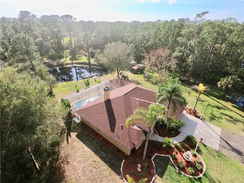 Aerial view of a wooded large-lot property with a pond and surrounding yard.