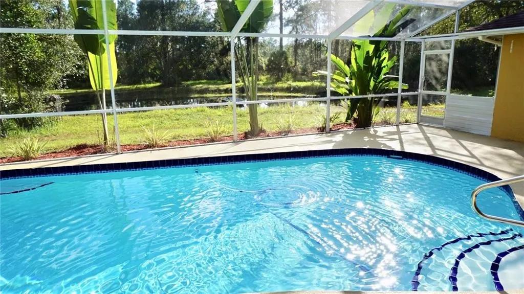 Screened pool, pond, trees, and a large-lot yard in a North Port Estates style setting.