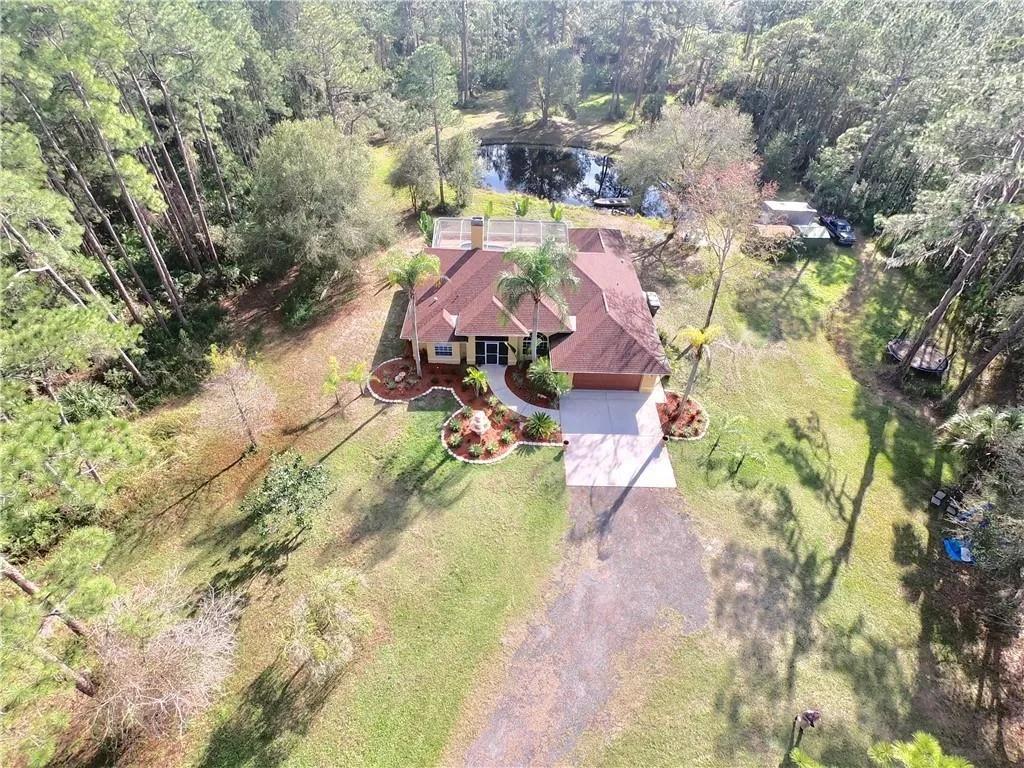 Aerial view of a large-lot property with a home, driveway, trees, and surrounding yard.